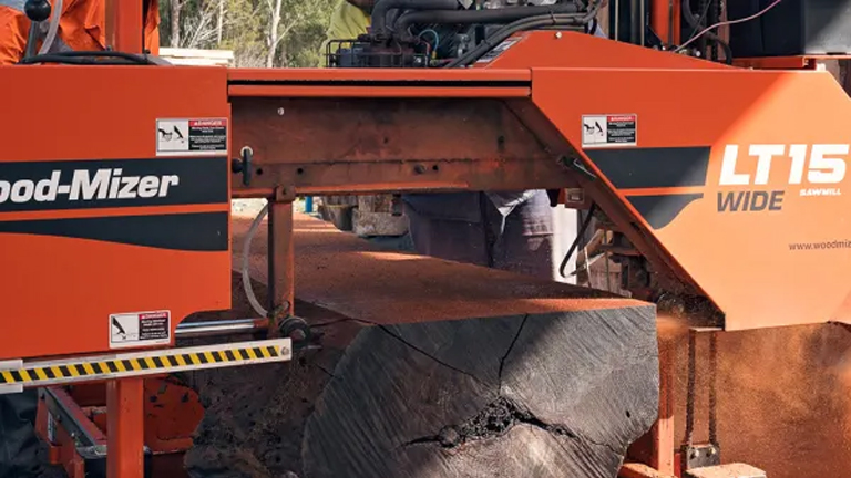 Orange Wood-Mizer LT15 WIDE Portable Sawmill cutting a log in a forested area