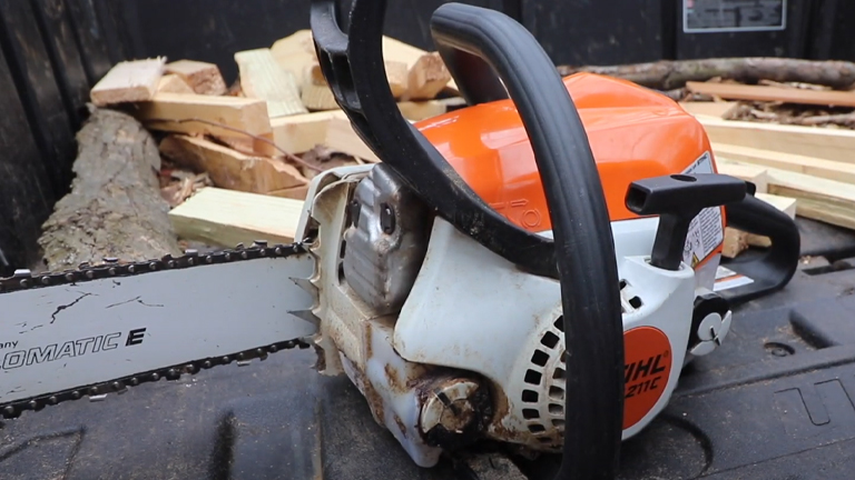 Stihl MS 211 Chainsaw with an orange and white body, resting on a black surface, surrounded by cut wood