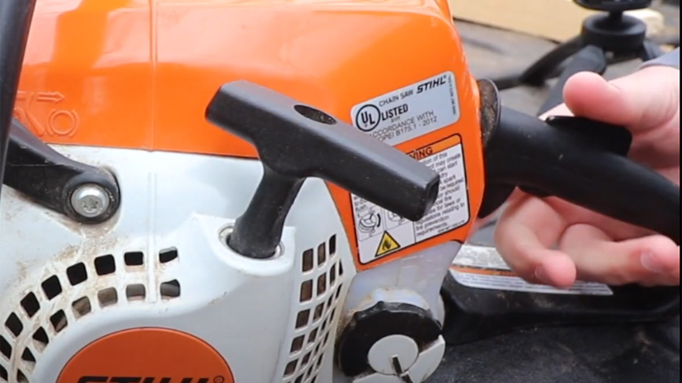 Close-up of a Stihl MS 211 Chainsaw with a person’s hand on the handle