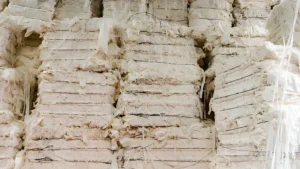 Stacks of large bales of cotton fiber bound with wire, stored in a warehouse.