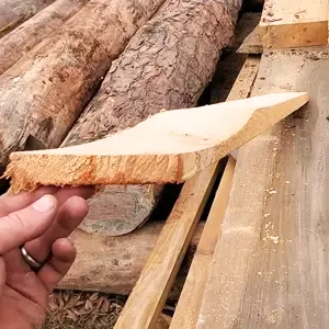 A hand holding a piece of wood with a rough cut, indicating the need to replace the sawmill blade