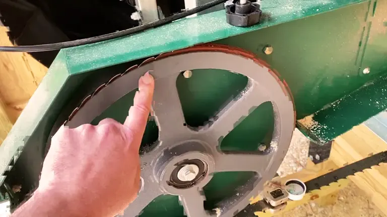 Person pointing at a worn sawmill blade attached to a green machine
