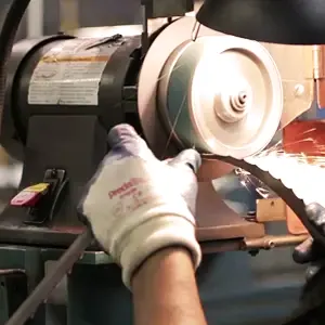 A person wearing gloves sharpening a sawmill blade