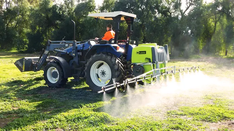 Blue tractor with a sprayer attachment applying treatment in a green field.