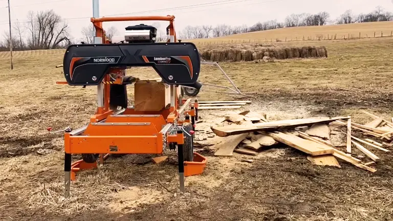 Sawmill sitting in a field next to a pile of wood. The sawmill is a Norwood LumberPro HD36V2.