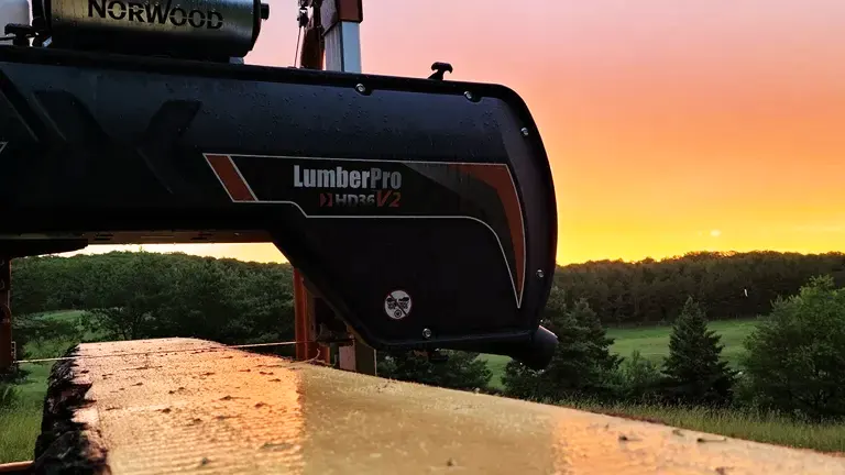 A Norwood LumberPro HD36V2 sawmill at sunset with trees in the background.
