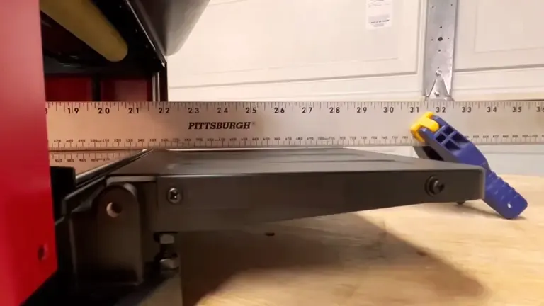 Close-up of a CRAFTSMAN Benchtop Planer with a PITTSBURGH measuring tape extended across it, on a wooden surface with a blue and yellow clamp beside it.