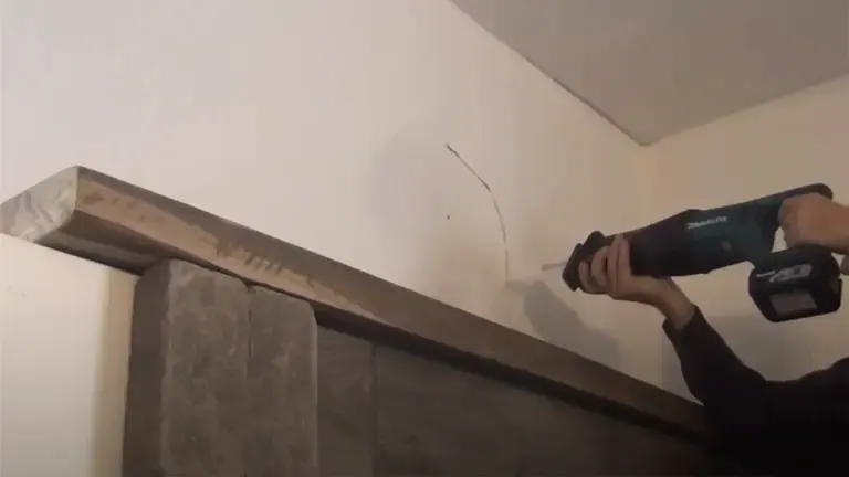 Person using a power drill to install a wooden mantle on an indoor wall.