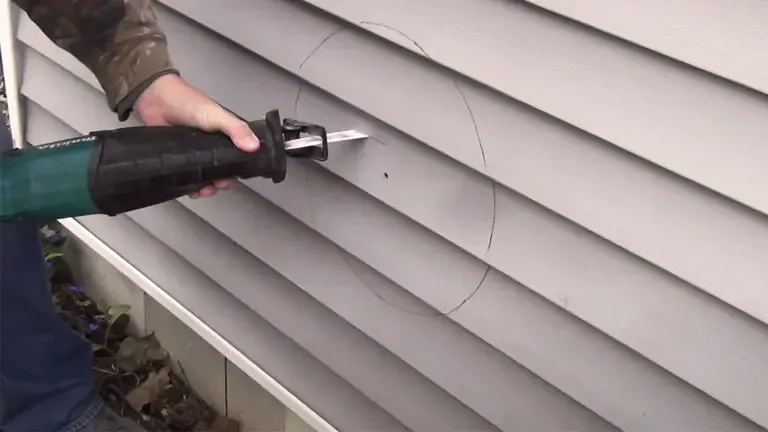 Person cutting circular marks on house siding with a power tool.