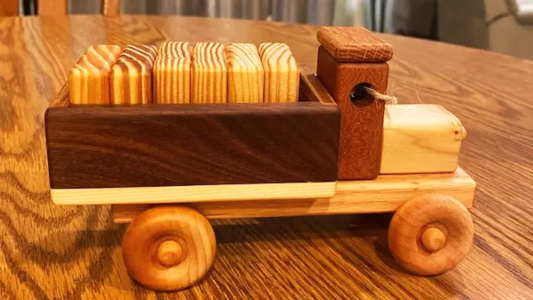 Wooden toy truck carrying cylindrical wooden pieces on a table.
