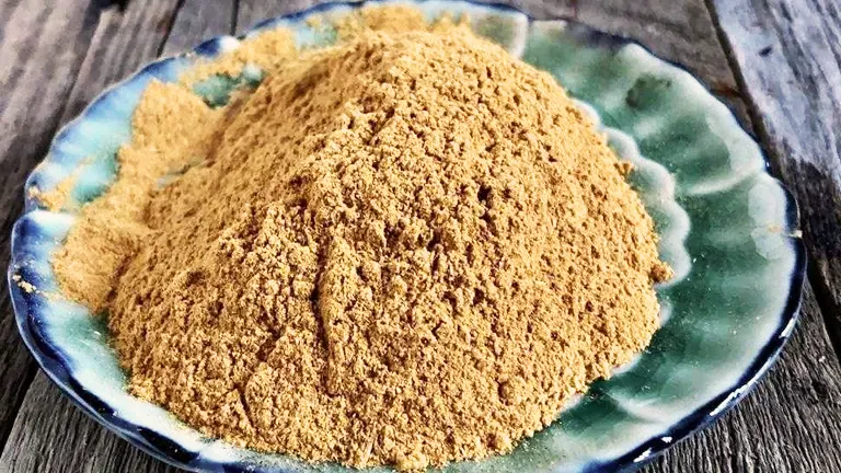 A mound of brown powder on a ceramic plate, displayed on a wooden surface.