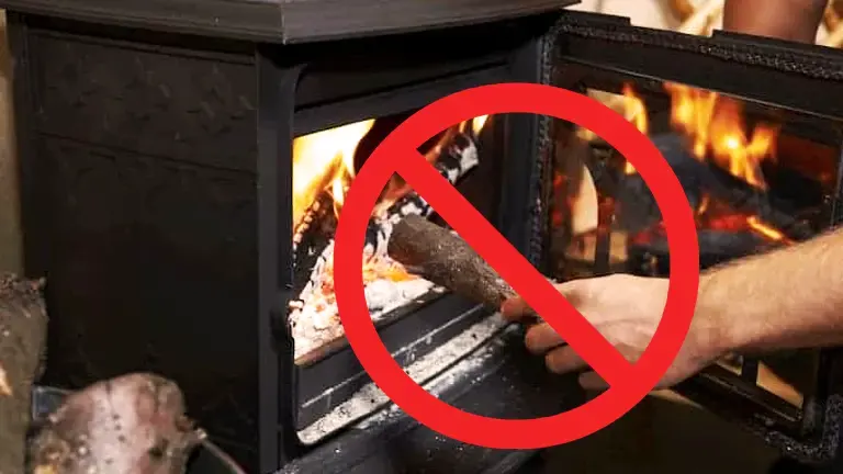 Person cleaning a wood stove, marked with a red circle and slash indicating not to do this.