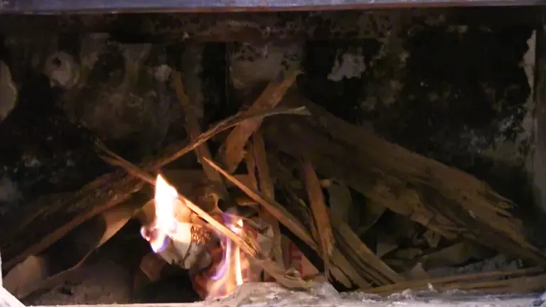 Fire burning in a wood stove with kindling stacked on top.