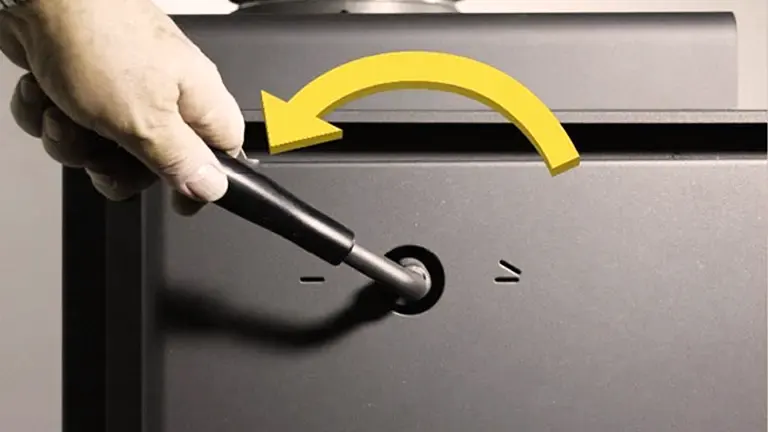 Hand turning a knob on a gray wood stove, indicated by a yellow arrow to the left.