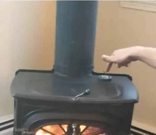 Person adjusting the control on a Vermont Castings wood stove with a glowing fire visible through the glass door