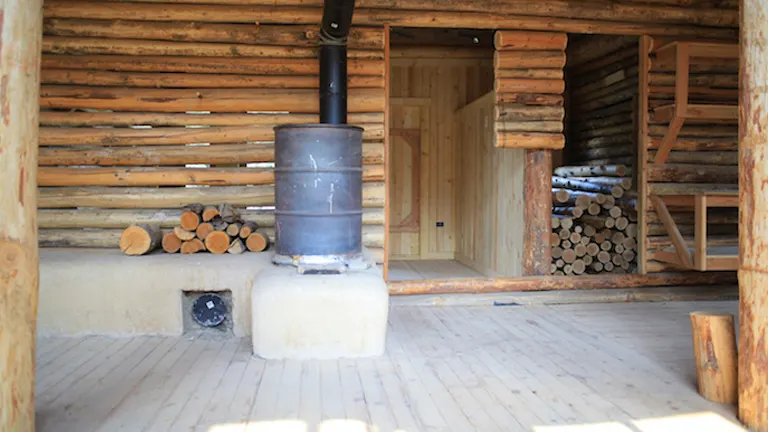 Log cabin interior with a wood-burning stove and stacked firewood.