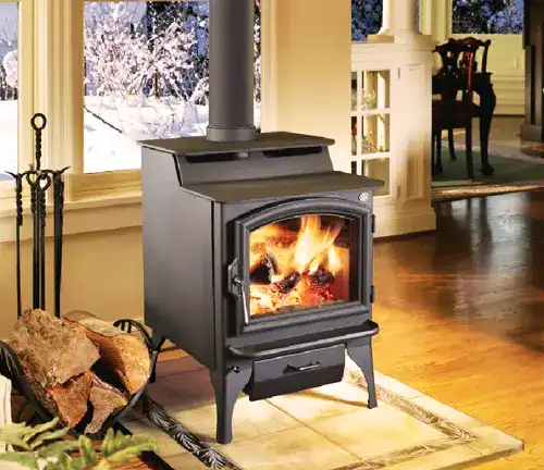 Indoor Lopi Endeavor NexGen-Fyre™ wood stove with visible fire, beside a window overlooking snowy landscape.