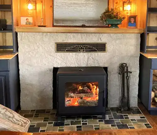 Black MF Fire Nova 2 wood stove in a cozy living room with stone fireplace, blue walls, and decorative elements.