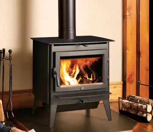 Lopi Evergreen wood stove with a burning fire, corner placement, wooden walls, log stack, and fireplace tools.