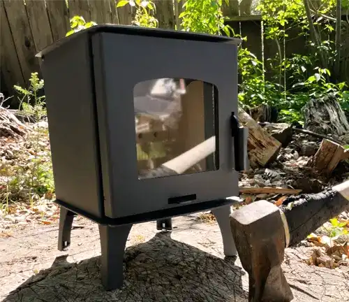 Mini wood stove outdoors on a log with an axe nearby