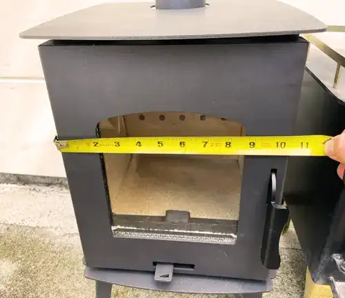 Person measuring the front opening of a Capybara Mini Wood RV Stove