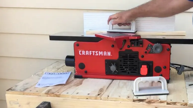 Hand pressing on red Craftsman wood jointer on wooden workbench.