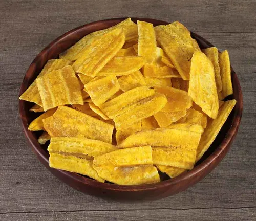 Bowl of crispy, yellow banana chips on a wooden surface