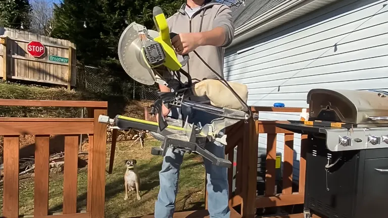 Person using a yellow and black Ryobi TSS103 10” Sliding Compound Miter Saw on a wooden deck with a dog in the background
