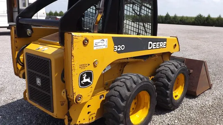 Yellow John Deere 320 skid steer loader with a bucket attachment on a gravel lot.