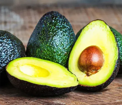 Three Hass avocados, one cut open, on a wooden surface