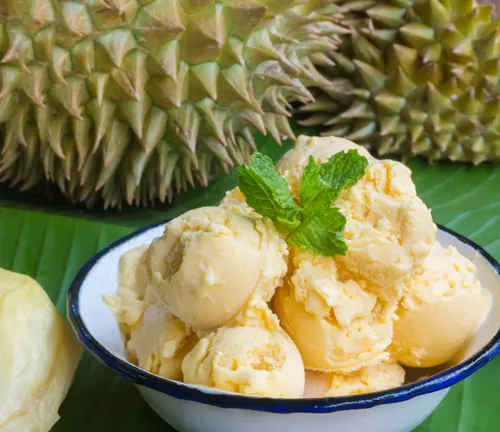 Bowl of durian ice cream garnished with mint, with whole durians in the background