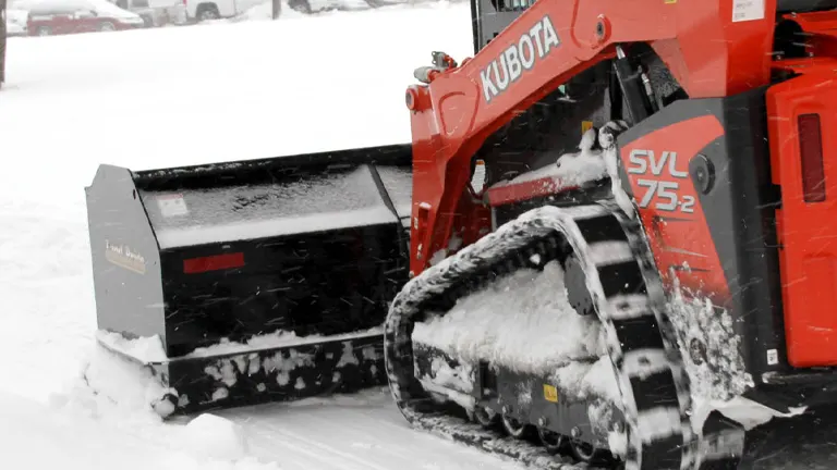 Red Kubota SVL75-2 snowplow clearing snow from a parking lot.