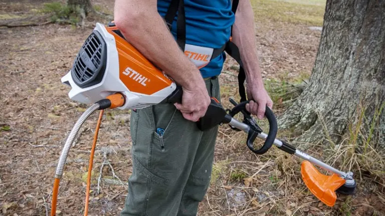 Person in gray outfit using an orange and white STIHL FSA 130 R Battery-Powered Trimmer in a garden