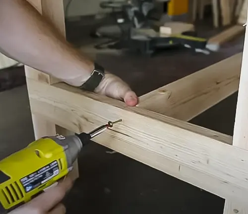 Person using a yellow drill to assemble a wooden frame for a miter saw station in a workshop