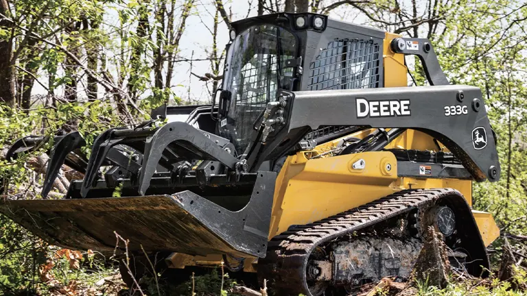 John Deere 333G compact track loader in a wooded area.