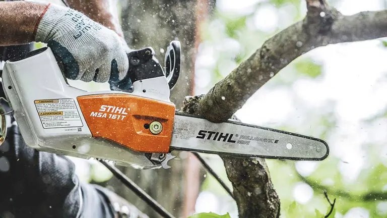 Person using a chainsaw to cut a tree branch.