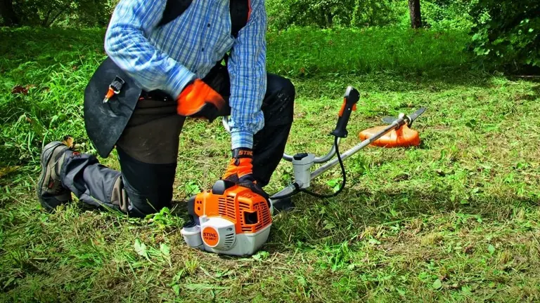 Person in gray outfit using an orange and white Stihl FS 240 Trimmer and Brushcutter in a garden