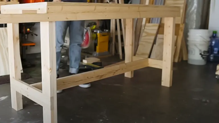 Incomplete wooden frame for a miter saw station in a workshop with tools and materials scattered around