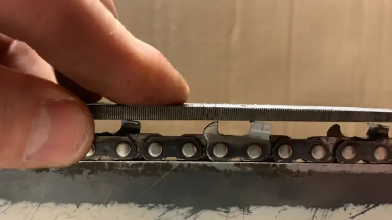 Close-up of a chainsaw chain being sharpened with a file on a metal surface