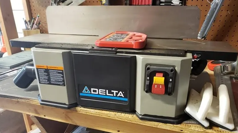 Delta wood jointer on workbench with tools in background.