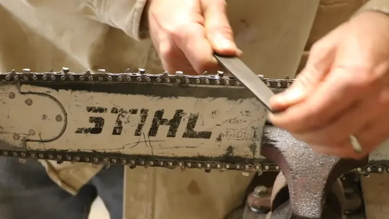 Close-up of a person sharpening a STIHL chainsaw with a file on a workbench in a workshop