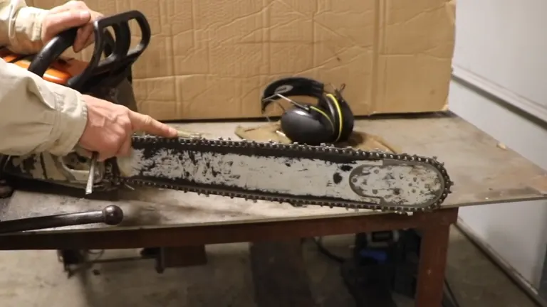 Person holding a chainsaw with a dirty chain on a workbench, safety headphones and gloves nearby