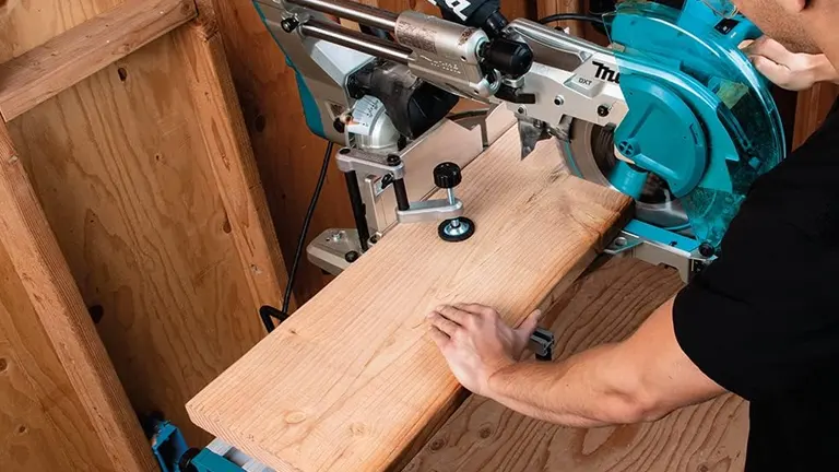 Person using Makita LS1219L 12" Dual-Bevel Sliding Compound Miter Saw on wooden plank.