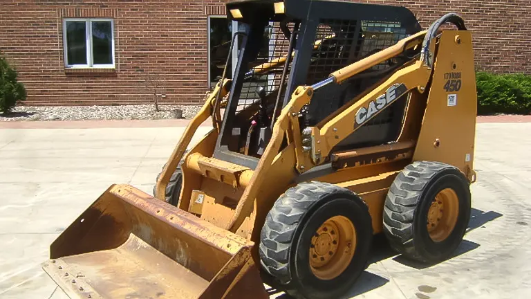 Yellow CASE 450 construction vehicle with a rusted bucket attachment parked in front of a brick building.