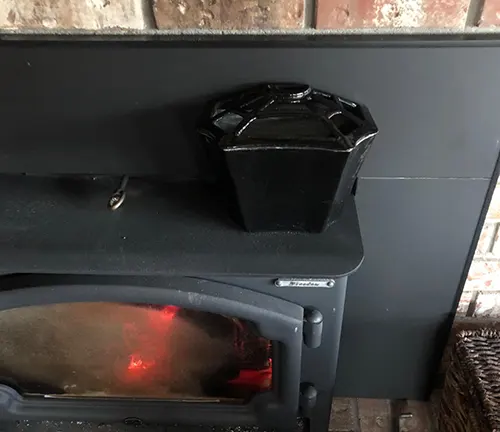 Black wood stove with a glowing red door and a black pot on top.