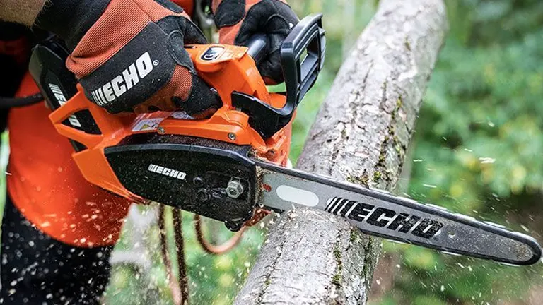 Person in black jacket using an orange chainsaw to cut a thick tree branch.