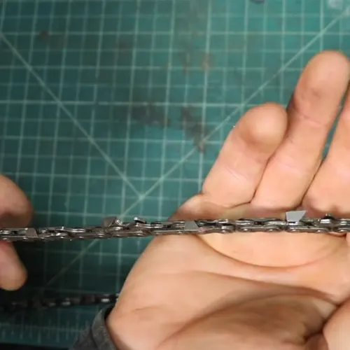 Hands holding a chainsaw chain on a green cutting mat