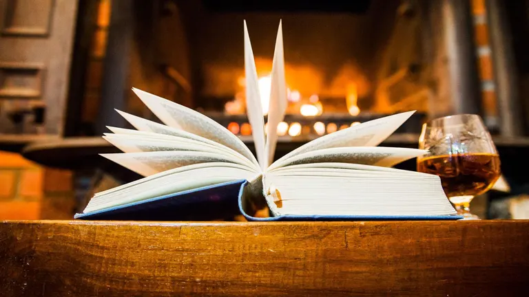 Open book and wine glass by a cozy fireplace.