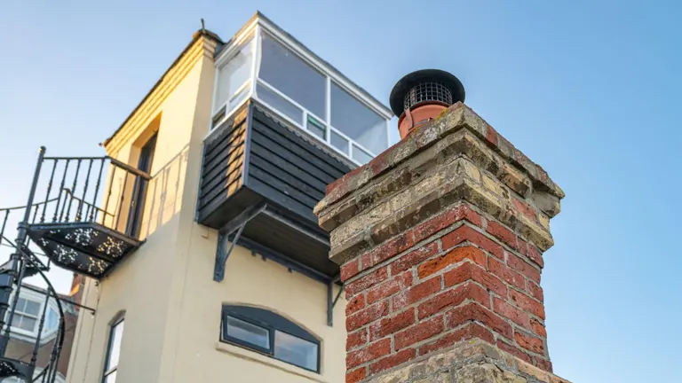 Brick chimney in front of a modern house with a balcony.