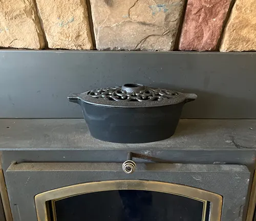 Black cast iron pot with a lid on a gray fireplace mantel.